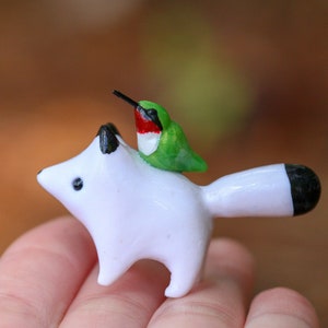 K&ouml;nnte beinhalten: Eine wei&szlig;e Keramik-Fuchsfigur mit schwarzer Schwanzspitze, ein kleiner gr&uuml;ner und roter Kolibri sitzt auf seinem R&uuml;cken.