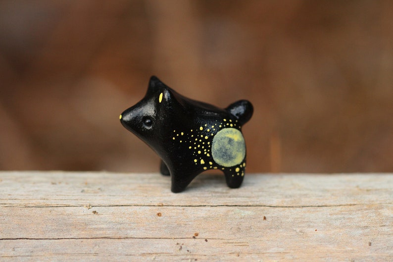 May include: A small black ceramic figurine of a dog with yellow painted spots and a yellow moon on its back.