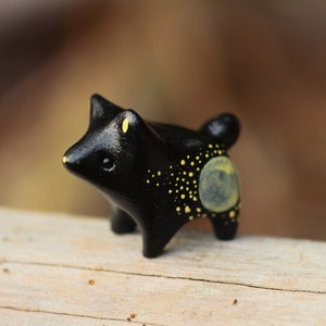 May include: A small black ceramic figurine of a wolf with yellow accents. The wolf has a round, yellow moon on its back with yellow dots scattered across its body.