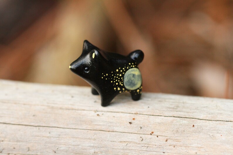 May include: A small black ceramic figurine of a fox with yellow painted spots and a moon on its back.