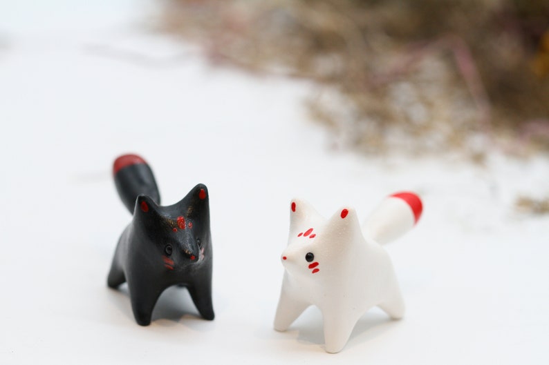 May include: Two small ceramic fox figurines, one black with red accents and one white with red accents.