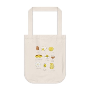 Könnte beinhalten: Eine weiße Einkaufstasche mit einer Cartoon-Illustration verschiedener Arten von Eiern, darunter ein Spiegelei, ein Rührei, ein pochiertes Ei und ein hartgekochtes Ei. Jedes Ei hat ein süßes Gesicht und ist mit seiner Zubereitungsart beschriftet. Der Text auf der Tasche lautet: "Lil' egg", "Lil' sunny", "Lil' scramble", "Lil' omelette", "Lil' devil", "Lil' just boiled", "Lil' poached", "Lil' hard boiled", und "Lil' tamago".