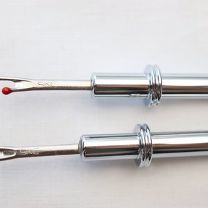 May include: Two silver thread snips with red tips. The snips have a retractable blade and a metal handle with a ring around the handle.