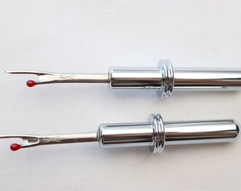 May include: Two silver thread snips with red tips. The snips have a retractable blade and a metal handle with a ring around the handle.