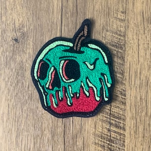 May include: A green and red embroidered patch of a melting apple with a skull inside. The apple is dripping green and red.