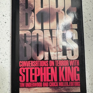 May include: A paperback book titled "Bare Bones" with the author's name, Stephen King, in large red letters. The cover is black with the title in large, textured, off-white letters. The book is about conversations on terror.