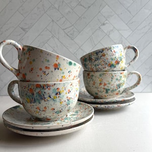 set of four  white ceramic teacup and saucer with a speckled pattern of yellow, orange, and green. latte mug