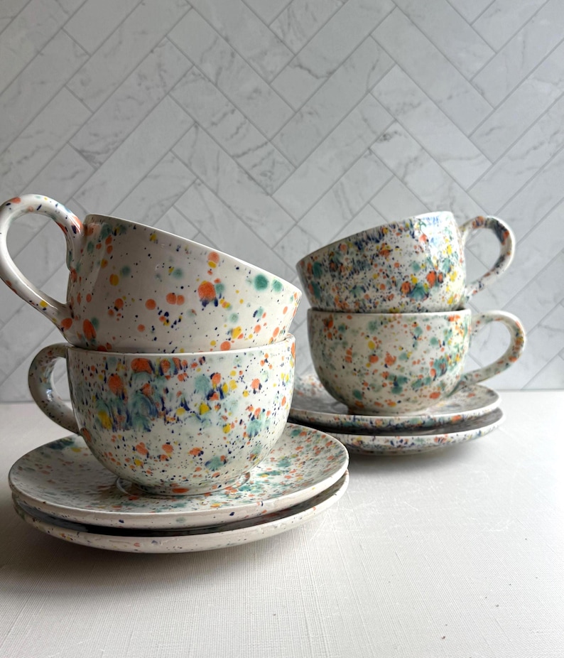 set of four  white ceramic teacup and saucer with a speckled pattern of yellow, orange, and green. latte mug