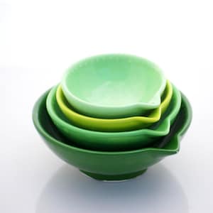 May include: A stack of four ceramic bowls in shades of green, from dark to light. Each bowl has a small spout. The bowls are nested, with the largest at the bottom and the smallest at the top.