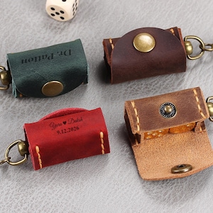 May include: Four small leather pouches with metal key ring attachments and snap closures. One green pouch is engraved with Dr. Patton, one red pouch with Yara heart Daksh 9.12.2026, and two brown pouches. One brown pouch is open, revealing dice inside.