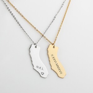 May include: Two gold and silver necklaces with California state-shaped pendants. The silver pendant has the initials "N.K.L." and a heart symbol engraved on it. The gold pendant has the Roman numerals "II.XXV.MMXVI" engraved on it.
