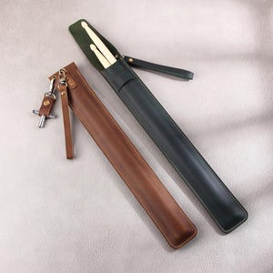May include: Two leather carrying cases for drumsticks. One case is brown leather and the other is green leather. Both cases have a strap.