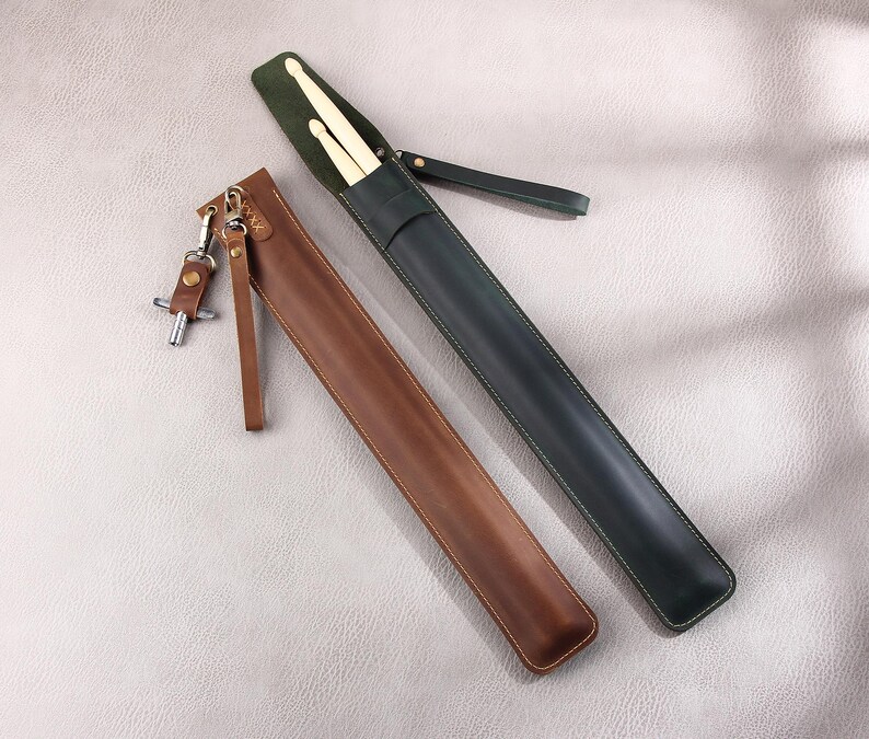 May include: Two leather carrying cases for drumsticks. One case is brown leather and the other is green leather. Both cases have a strap.