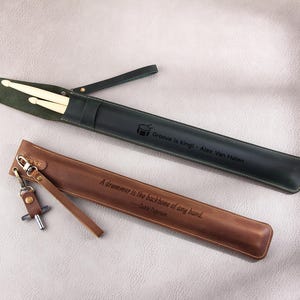 May include: Two leather drumstick holders. One is green with the text "Groove is king! - Alex Van Halen" and the other is brown with the text "A drummer is the backbone of any band. - Debbi Peterson".