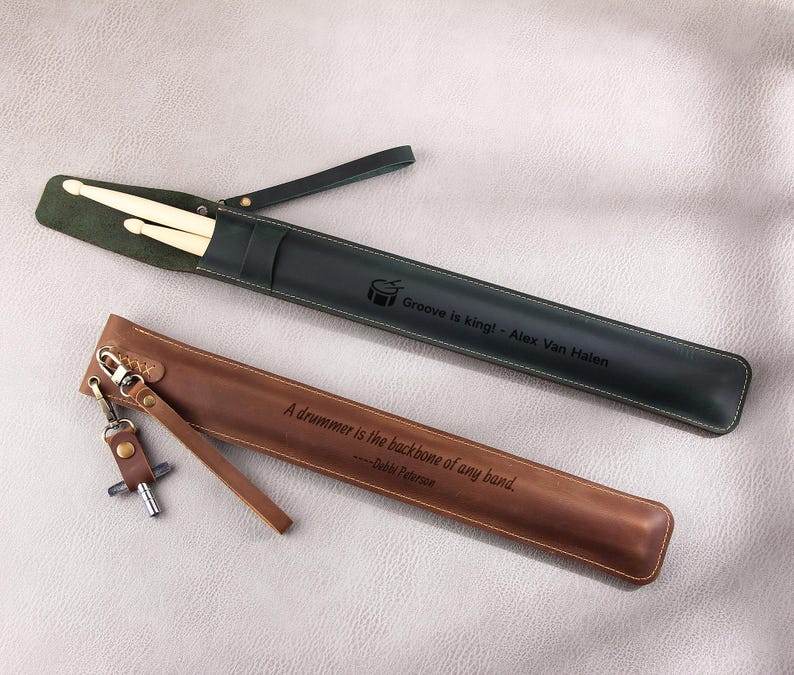 May include: Two leather drumstick holders. One is green with the text "Groove is king! - Alex Van Halen" and the other is brown with the text "A drummer is the backbone of any band. - Debbi Peterson".