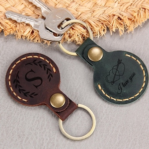 May include: Two leather keychains with metal rings. One is dark brown with an initial "S" and a laurel wreath design. The other is dark green with a heart and arrow design and the text "I love you".