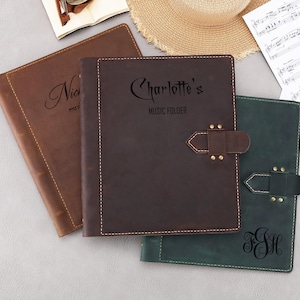 Peut inclure: Trois pochettes à musique en cuir avec des noms personnalisés. Les pochettes sont marron, marron foncé et verte. Les pochettes ont un rabat avec une fermeture à boucle. Le texte sur les pochettes est "Nicholas", "Charlotte's Music Folder" et "F.S.H."