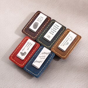 May include: Six different leather money clips with engraved metal plates. The plates have various messages, including "I need you to be here with me", "My reliance, my guide, my teacher, my hero, I love you", "It's time to write. Start recording your journey by now", "My first Father's Day, 7th of July 2017", "The journey is my compass, the adventure is my guide", and "Paige George 4.30.2019".