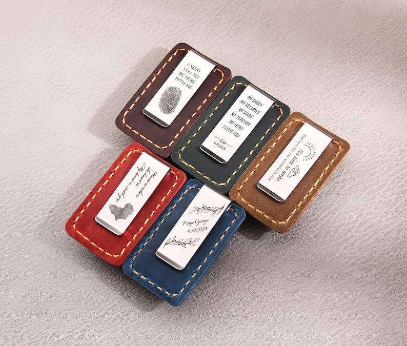 May include: Six different leather money clips with engraved metal plates. The plates have various messages, including "I need you to be here with me", "My reliance, my guide, my teacher, my hero, I love you", "It's time to write. Start recording your journey by now", "My first Father's Day, 7th of July 2017", "The journey is my compass, the adventure is my guide", and "Paige George 4.30.2019".
