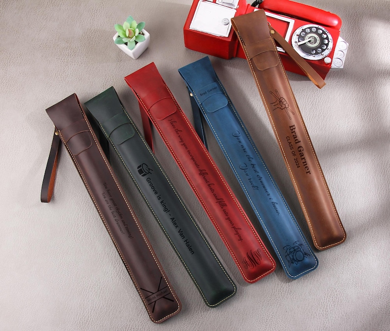 May include: Five leather carrying cases with different engraved messages. The cases are in various colors, including brown, red, blue, and green. The text on the cases includes "Brad Garner, Class of 2024", "You are the best driver I know", "Groove is King - Alex Van Halen", and "You are the best driver I know".