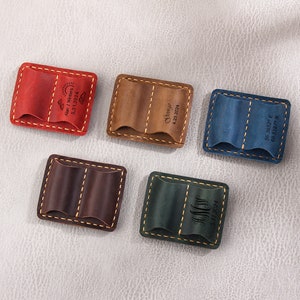 Puede incluir: Cinco bolsas de cuero con bordes cosidos y grabados personalizados. Las bolsas son de color rojo, marrón, azul, verde y marrón oscuro.