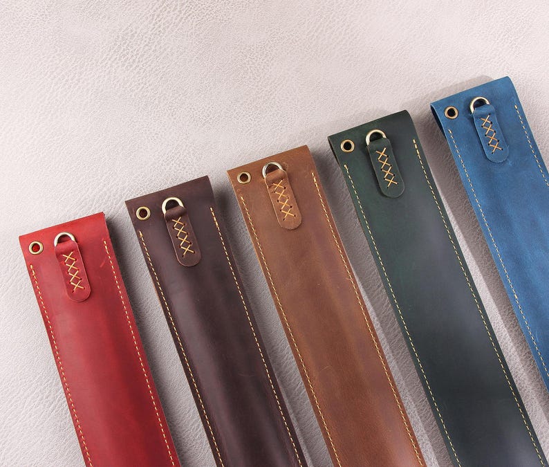 May include: Six leather pen cases in different colors, including red, brown, dark brown, blue, and green. Each case has a gold metal ring and a stitched design.