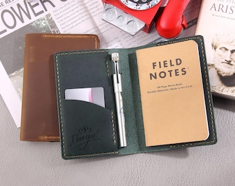 May include: A brown and green leather notebook cover with a pen holder and a card slot. The cover is closed and the notebook inside is a Field Notes brand memo book. The cover has the words "I love you!" engraved on the front.