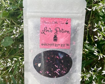 May include: A white pouch with a pink label that says "Becca's Little Teas" and "Love Potion" in black text. The label also has a small teacup icon and a bottle with hearts. The pouch contains loose leaf tea.