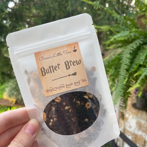 May include: A white resealable pouch with a label that reads "Becca's Little Teas" and "Butter Brew Handcrafted Loose Leaf Tea". The pouch contains loose leaf tea with brown, black, and white pieces.