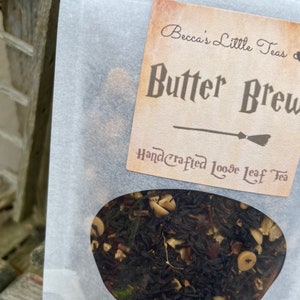 May include: A white paper bag with a label that reads "Becca's Little Teas" and "Butter Brew Handcrafted Loose Leaf Tea". The bag contains loose leaf tea.