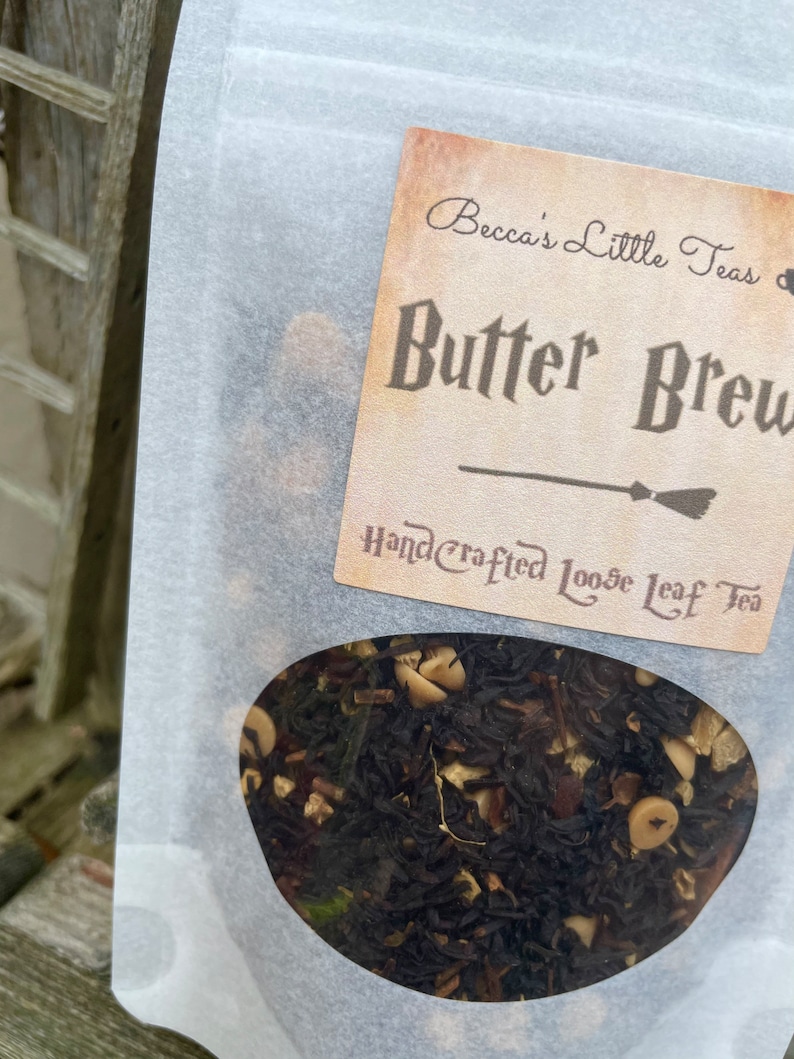 May include: A white paper bag with a label that reads "Becca's Little Teas" and "Butter Brew Handcrafted Loose Leaf Tea". The bag contains loose leaf tea.