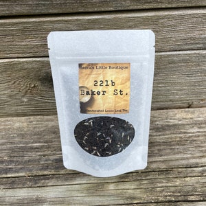 May include: A white pouch with a label that reads "Becca's Little Boutique 221b Baker St. Handcrafted Loose Leaf Tea". The pouch contains loose leaf tea.