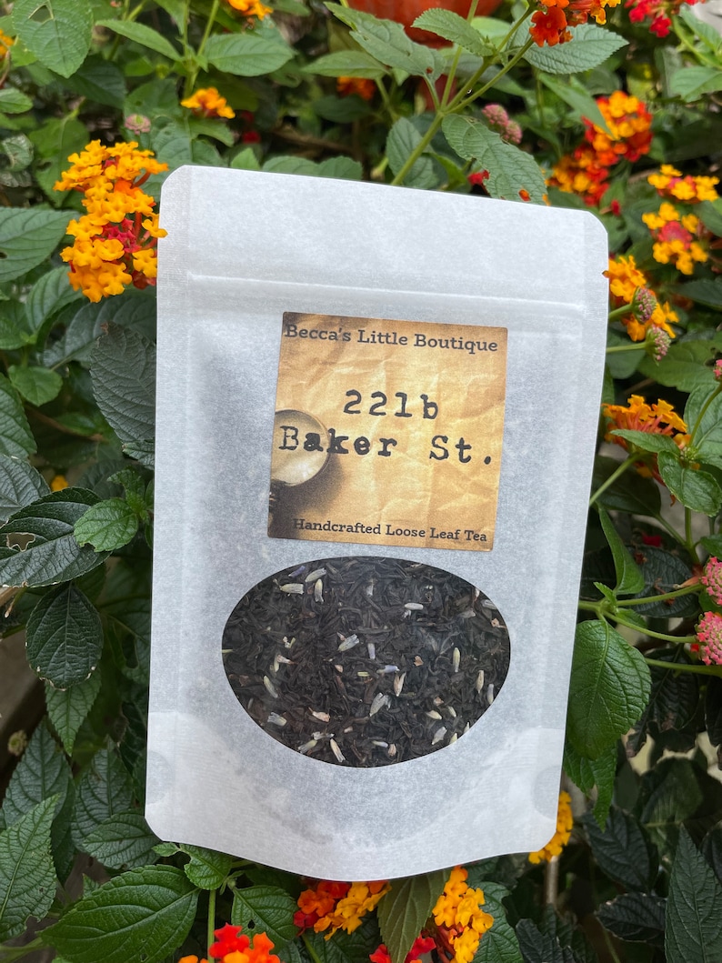 May include: A white paper bag with a label that reads "Becca's Little Boutique 221b Baker St. Handcrafted Loose Leaf Tea". The bag contains loose leaf tea.