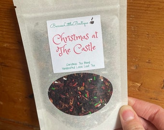 May include: A white pouch with a label that reads "Christmas at the Castle" and "Christmas Tea Blend Handcrafted Loose Leaf Tea". The pouch contains loose leaf tea with red, green, and white sprinkles.