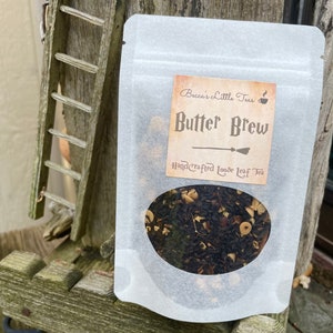 May include: A white resealable pouch with a label that reads "Becca's Little Teas" and "Butter Brew Handcrafted Loose Leaf Tea". The label has a brown background with a black and white illustration of a broom.