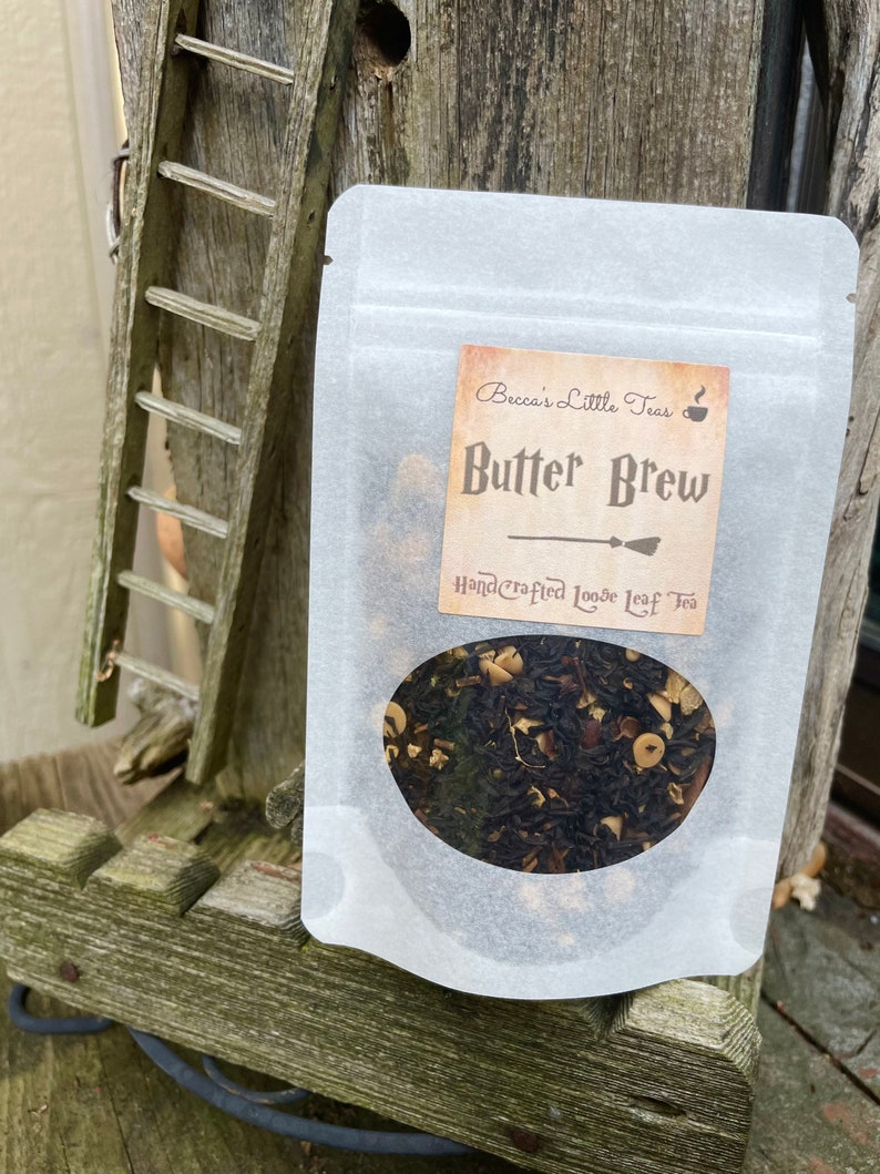 May include: A white resealable pouch with a label that reads "Becca's Little Teas" and "Butter Brew Handcrafted Loose Leaf Tea". The label has a brown background with a black and white illustration of a broom.