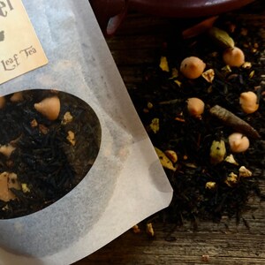May include: Close-up of a white paper bag with a round window showing loose leaf black tea with chocolate chips and other ingredients. The bag has the text "Loose Leaf Tea" printed on it.