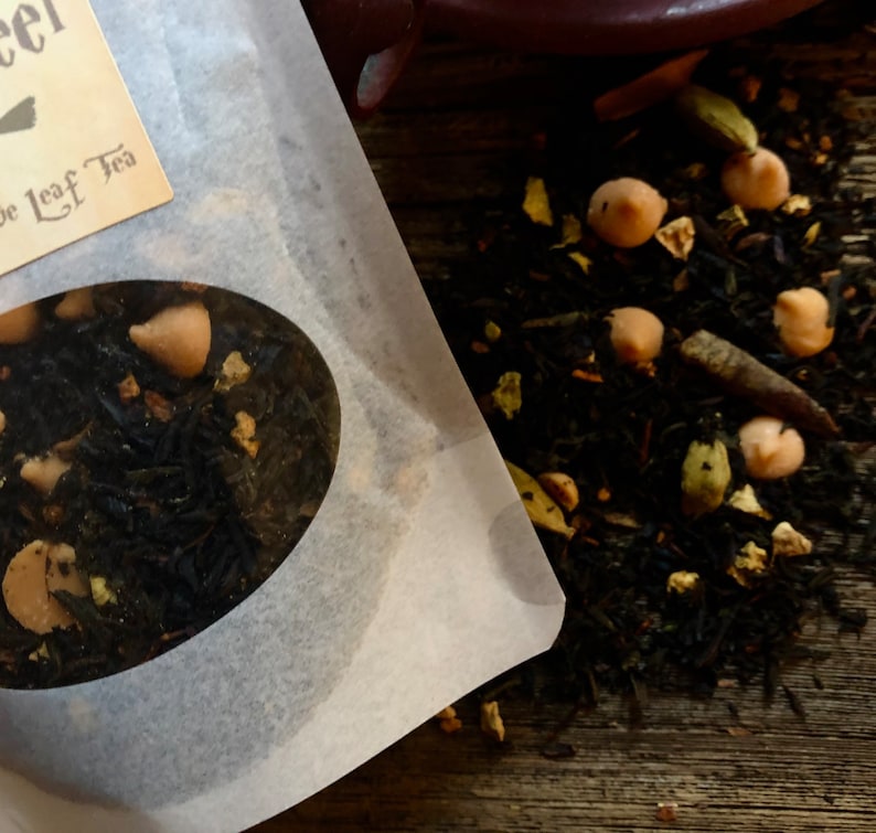 May include: Close-up of a white paper bag with a round window showing loose leaf black tea with chocolate chips and other ingredients. The bag has the text "Loose Leaf Tea" printed on it.