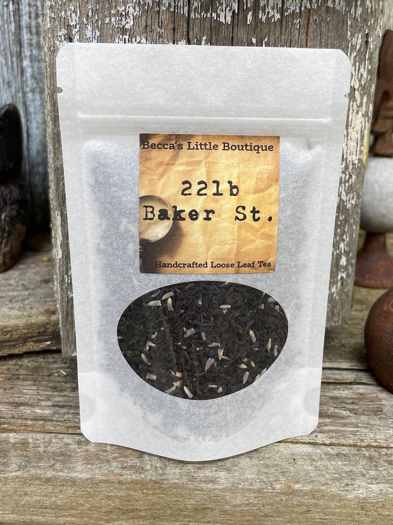 May include: A white paper bag with a label that reads "Becca's Little Boutique 221b Baker St. Handcrafted Loose Leaf Tea". The bag contains loose leaf tea.