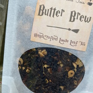 May include: A white paper bag with a clear window showing loose leaf tea. The bag has a label that reads "Becca's Little Teas" and "Butter Brew" in a dark brown font. The label also says "Handcrafted Loose Leaf Tea" in a smaller font.