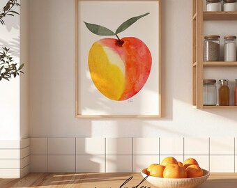 May include: A framed wall art print featuring a watercolor illustration of a single peach with a yellow and red gradient and two green leaves. The artwork is displayed on a white wall above a wooden counter with a bowl of fresh oranges.