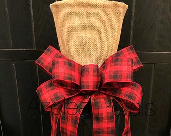 May include: A red and black plaid bow with burlap on top, tied around a black lantern.