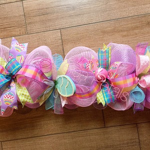 May include: A pink, purple, blue and green Easter wreath with bows and egg-shaped decorations.