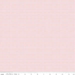 May include: A light pink fabric with a small, grid-like pattern. The fabric has a subtle texture and a soft, pastel color. The image includes a ruler at the bottom with inch measurements. The fabric is from Riley Blake Designs.
