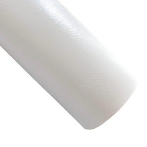 May include: A roll of white, textured material, possibly leather or vinyl, is angled across the frame. The material has a subtle sheen, reflecting light. The surface appears smooth with a slight grain.