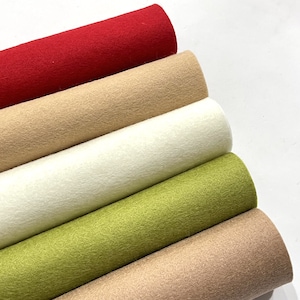 May include: Five rolls of felt fabric in different colours: red, beige, white, green, and beige. The rolls are stacked on top of each other.