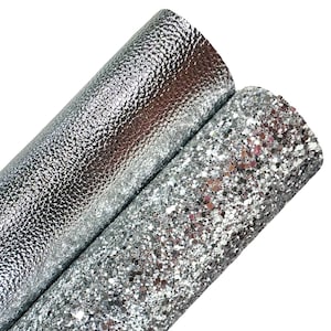 Peut inclure: Deux rouleaux de simili cuir argenté. L'un a une surface texturée et granuleuse, tandis que l'autre est recouvert de paillettes argentées scintillantes. Les rouleaux sont inclinés, mettant en valeur les différentes textures.