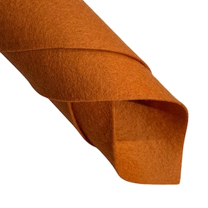 May include: Close-up of a rolled-up sheet of orange felt. The felt is a solid colour with a slightly textured surface. The edges of the felt are visible, showing the layers of the material. The felt is against a white background.