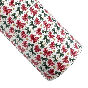May include: A roll of white faux leather fabric with a repeating pattern of red and green bows and gold stars. The bows are detailed with watercolor-style shading. This fabric is suitable for crafting and holiday-themed projects.