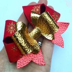 Könnte beinhalten: Eine festliche Haarschleife mit rotem Band und goldenen Schneeflocken-Akzenten. Die Schleife hat eine goldfarbene Metallmitte und eine strukturierte rote Basis, wodurch ein geschichteter Effekt entsteht. Dieses Accessoire zum Thema Feiertage verleiht Glanz.